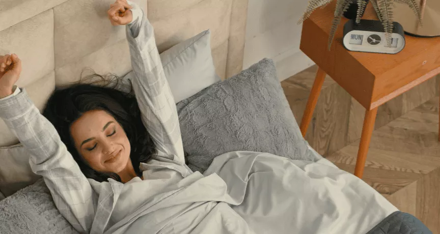 A imagem mostra uma mulher em uma cama, se espreguiçando ao acordar 