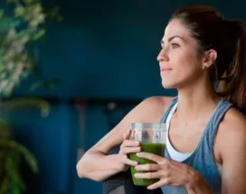 Imagem mostra uma mulher branca tomando um suco verde 