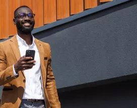 homem "CLT premium" feliz andando na rua enquanto segura o celular.