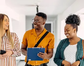 três pessoas conversando e rindo em corredor.