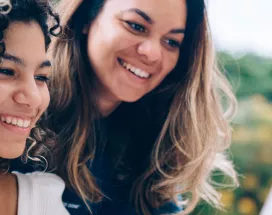duas mulheres sorrindo enquanto olham algo em computador ao ar livre.