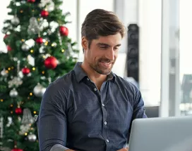 homeme trabalhando com árvore de natal atrás.