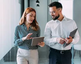 duas pessoas conversando enquanto olham dado em tablet dentro de uma empresa.