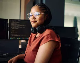 mulher sentada olhando para a câmera com monitores ao fundo.