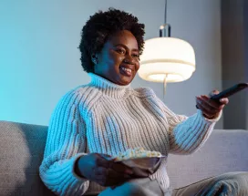 mulher em sofá segurando um balde de pipoca e controle remoto.