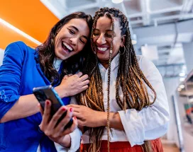 duas mulheres rindo enquanto olham algo em celular.