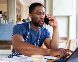 dono de empresa falando no telefone enquanto usa notebook.