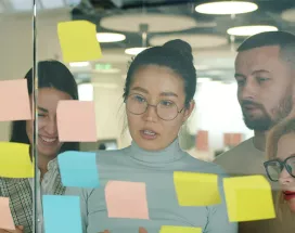 grupo de pessoas olhando para notas autoadesivas em parede de vidro.