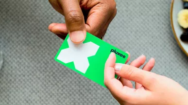 Mulher usa o cartão de benefício Pluxee para pagar uma conta. Nossos cartões são feitos com plástico reciclável!