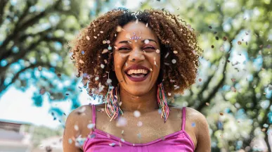 Foto mostra mulher sorridente pulando Carnaval numa praça