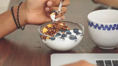 Foto mostra uma tigela de iogurte que uma pessoa está comendo durante o trabalho