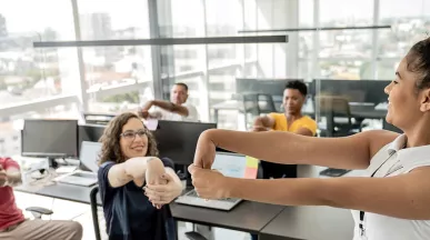 Quatro trabalhadores fazem ginástica laboral no escritório com uma professora