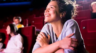 Mulher sorri e assiste com atenção a um filme no cinema