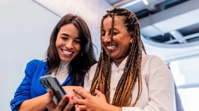 Duas amigas de trabalho conferem no celular os benefícios para funcionários que recebem da empresa