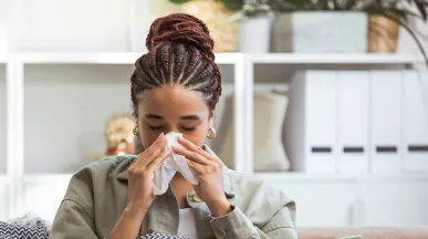 Foto mostra uma mulher assoando o nariz porque está resfriada 