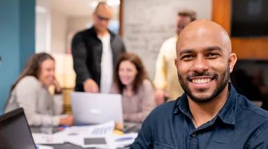 Foto mostra uma equipe de trabalho, com um homem sorrindo em destaque na frente