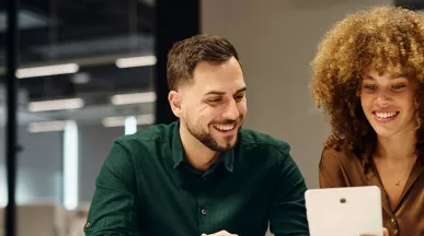 um homem e uma mulher sorrindo olhando para tablet.