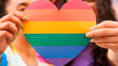 Foto mostra duas pessoas segurando um coração de arco-íris