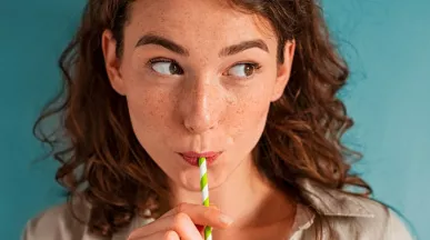 Foto mostra uma mulher tomando uma bebida de canudinho