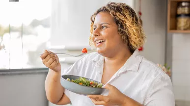 mulher comendo salada sorrindo.
