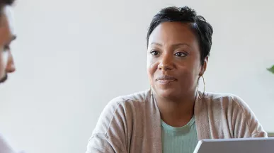 homem conversando com mulher que senta atrás de um notebook.