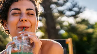 A imagem mostra uma mulher tomando suco enquanto toma um banho de sol.