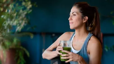 Imagem mostra uma mulher branca tomando um suco verde 