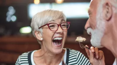 A imagem mostra um casal com cabelos grisalhos se alimentando em um restaurante