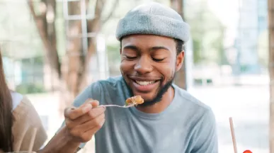 A imagem mostra um rapaz e uma mulher se alimentando ao ar livre