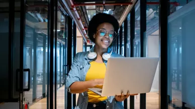 mulher sorrindo enquanto segura computador e caminha em um corredor de escritório.