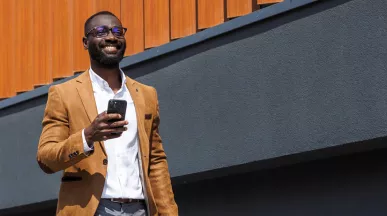homem "CLT premium" feliz andando na rua enquanto segura o celular.