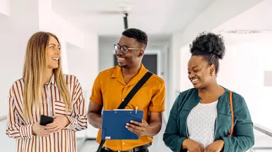 três pessoas conversando e rindo em corredor.