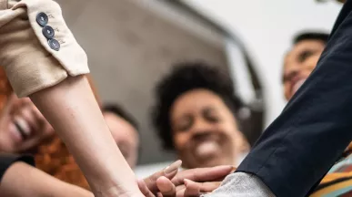 A imagem mostra um grupo de trabalhadores juntando as mãos e celebrando