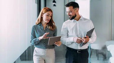 duas pessoas conversando enquanto olham dado em tablet dentro de uma empresa.