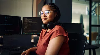 mulher sentada olhando para a câmera com monitores ao fundo.