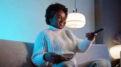 mulher em sofá segurando um balde de pipoca e controle remoto.