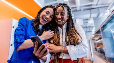 duas mulheres rindo enquanto olham algo em celular.