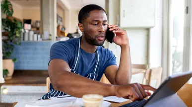 dono de empresa falando no telefone enquanto usa notebook.