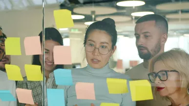 grupo de pessoas olhando para notas autoadesivas em parede de vidro.