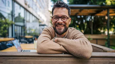 Homem sorrindo de braços cruzados no ambiente corporativo