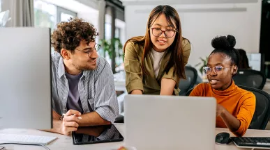 três pessoas conversando enquanto olham algo em computador.
