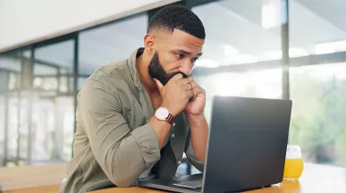 Foto mostra um homem preocupado olhando para seu notebook no escritório