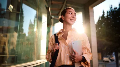 Foto de uma jovem profissional na área externa da empresa em que trabalha