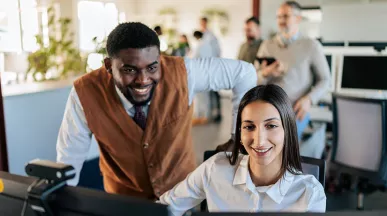 um homem e uma mulher sorrindo olhando para computador em escritório.