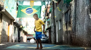 Foto mostra um menino jogando bola em uma rua enfeitada para a Copa do Mundo