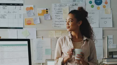 mulher segurando xícara de café em frente a uma série de papéis com planejamento estratégico.