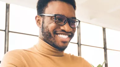 Homem negro, de camiseta amarela olhando para o notebook e sorrindo
