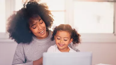 mãe e filha sorrindo enquanto olham algo no computador.