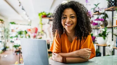 dona de floricultura sorrindo com computador.