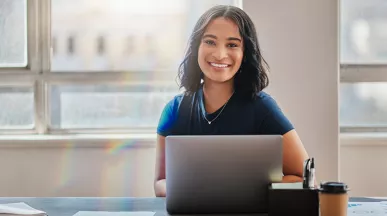 mulher sorrindo para a câmera enquanto usa notebook.